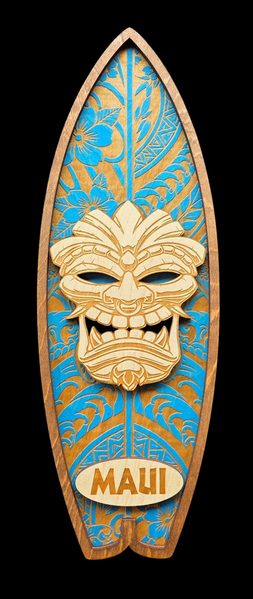 Wooden surfboard-shaped decorative item with Tiki mask design and 'Maui' text on a black background