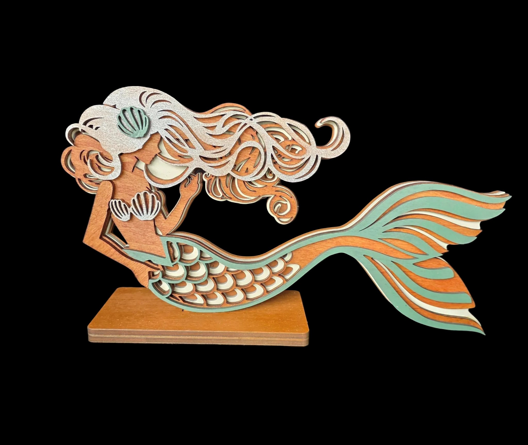 Wooden mermaid figurine with a teal tail and brown hair on a dark fabric background