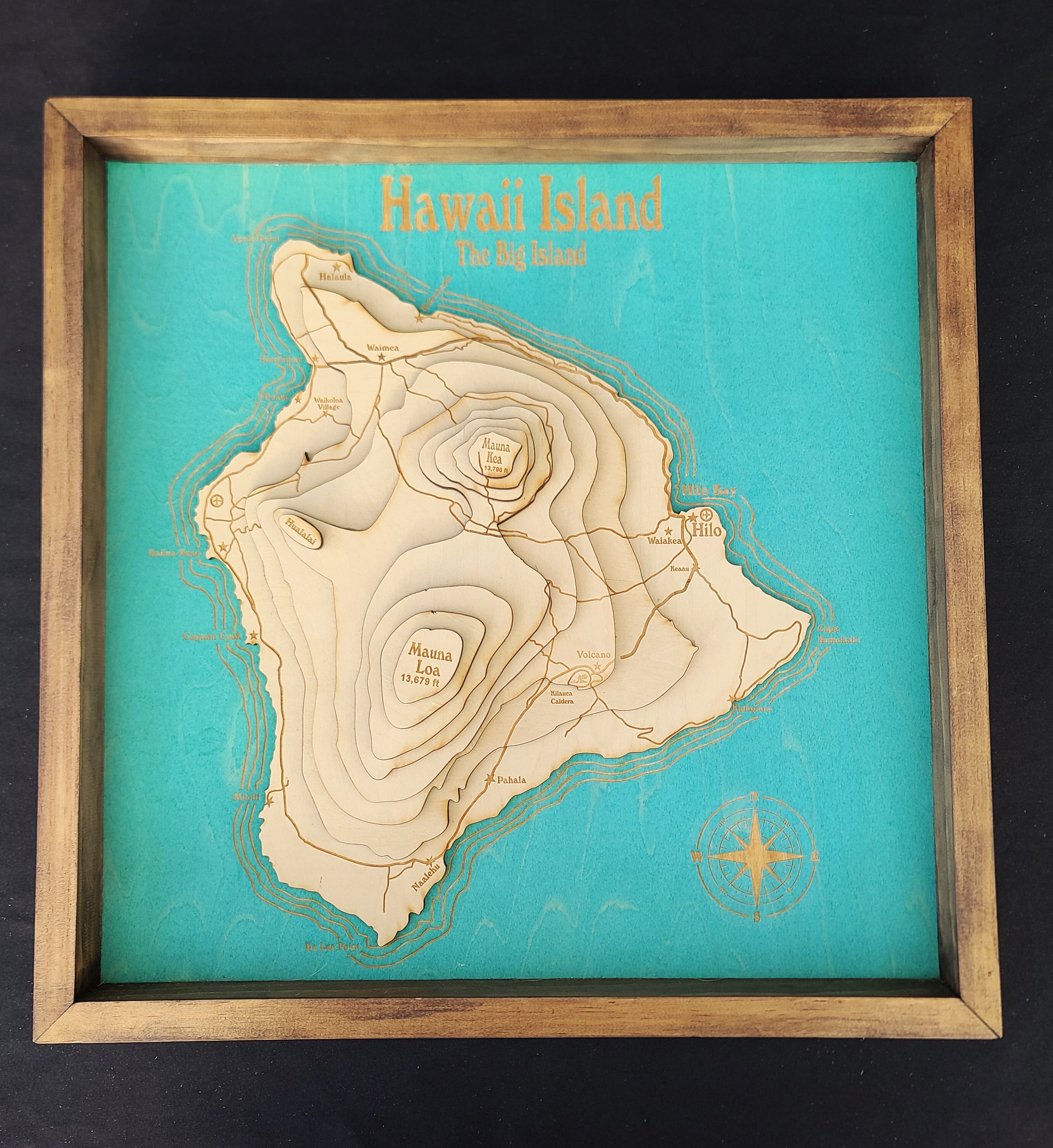 Wooden map of Hawaii Island on a teal background with a wooden frame.
